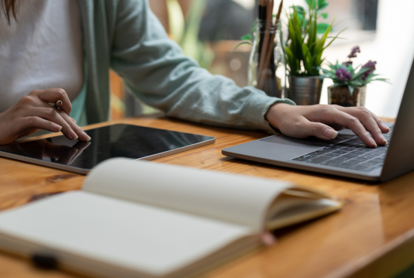 Person working on laptop and tablet with notebook open